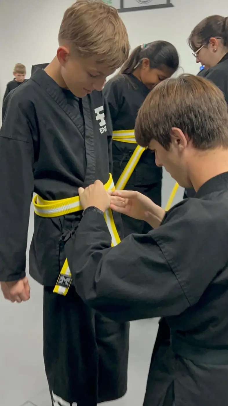 Coach tying a yellow belt on a student at Engage Lifestyle Martial Arts
